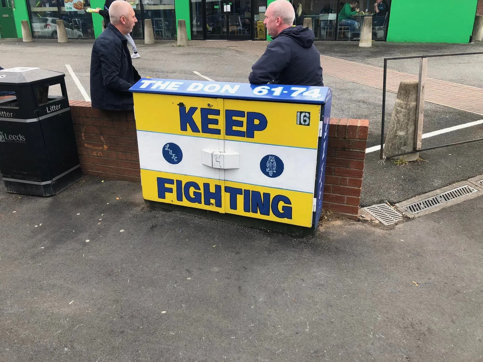 Yellow, white and blue Keep Fighting sign with Leeds United badges outside The Don pub near Elland Road